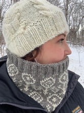 Load image into Gallery viewer, A woman stands in a snowy field wearing a white knit hat and a gray knit cowl with a colorwork motif of white flowers.
