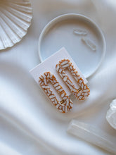 Load image into Gallery viewer, A pair of tortoise style hair clips in cream and thin brown lines lay on a white table cloth and saucer.
