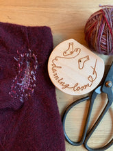 Load image into Gallery viewer, A wood darning loom lies next to a mended maroon knit sweater, ball of yarn, and steel scissors.
