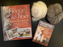 Load image into Gallery viewer, The Fleece and Fiber Sourcebook, a large hardcover, lies next to The Field Guide to Fleece, a small pocket-size softcover with a picture of natural fibers and roving on its cover. A ball of gray yarn with white speckles, and white wool roving, lie nearby.
