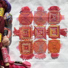 Load image into Gallery viewer, The Log Cabin Embroidery Sampler is a pre-printed pattern with red brush strokes, stitched on top with various colors of embroidery and fringe. Embroidery threads lay nearby.
