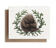 Load image into Gallery viewer, A greeting card made of seed paper depicts an illustration of a fat, happy porcupine sitting surrounded by evergreen boughs.
