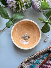 Load image into Gallery viewer, Terra cotta ceramic bowl holding silver acorn stitch markers.
