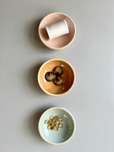Load image into Gallery viewer, Three ceramic notions bows in pale pink, terra cotta, and sky blue, holding spool of thread, buttons and gold stitch markers.
