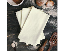 Load image into Gallery viewer, three natural flour sack towels on a baking surface surrounded by flour,muffins and wood spoons.
