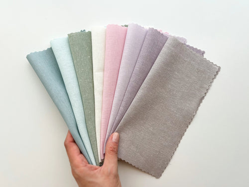 A hand holds eight pastel linen-cotton blend fabrics.