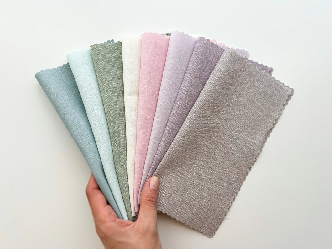 A hand holds eight pastel linen-cotton blend fabrics.