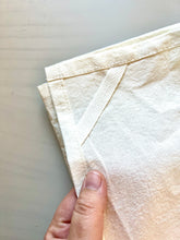 Load image into Gallery viewer, A hand holds the corner of a natural cotton flour sack towel with hanging loop.
