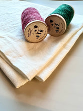 Load image into Gallery viewer, Two spools of woo thread in dark pink and turquoise rest atop a folded natural cotton flour sack towel.
