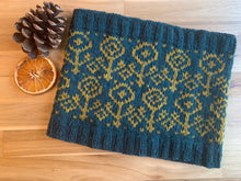 Load image into Gallery viewer, A dark aqua colored knit cowl with mustard yellow colorwork flowers, lying on a table next to a pinecone and dried orange slice.
