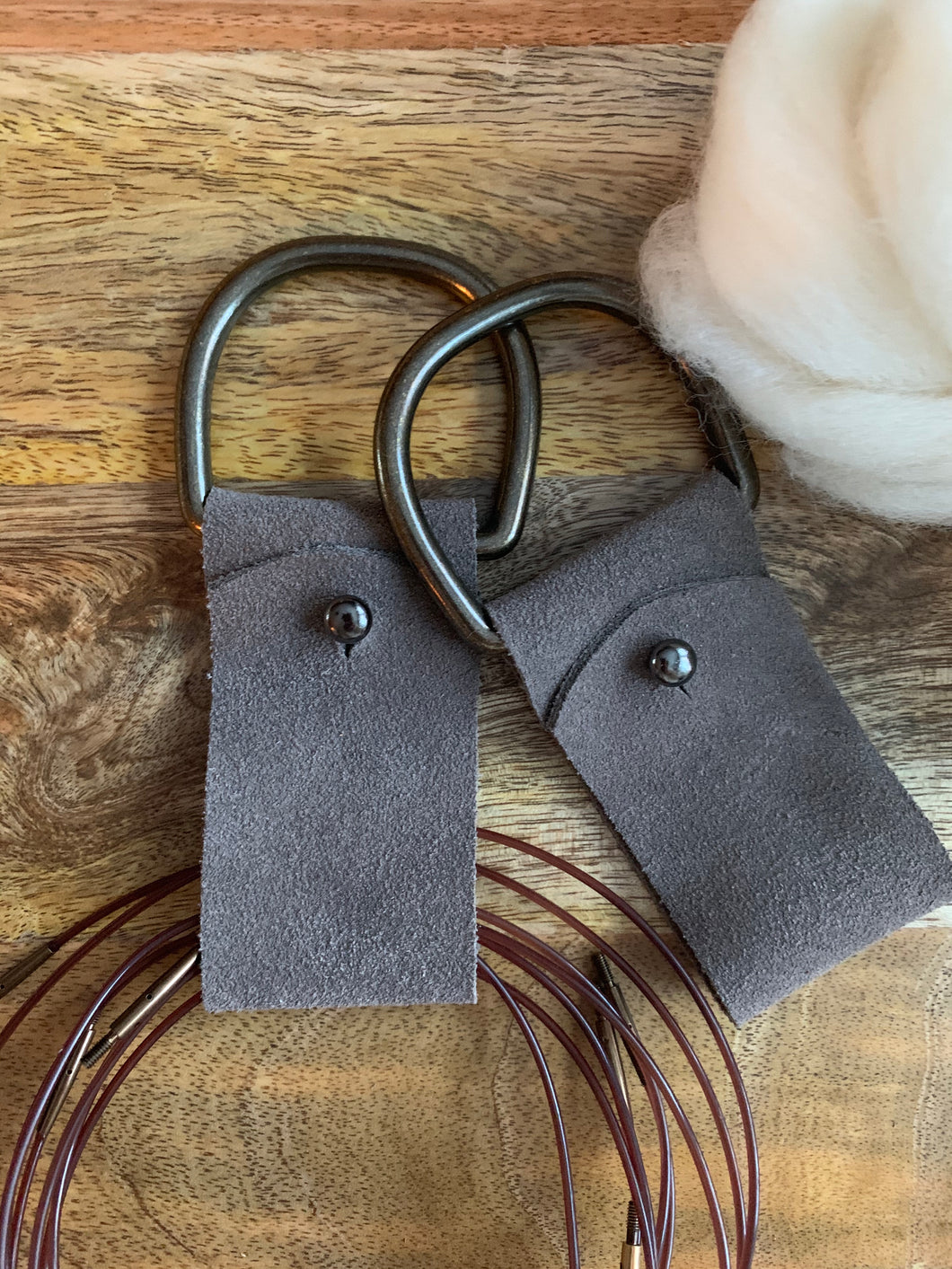 Circular knitting needle holders in gray suede - made of a brass D ring, leather loop, and clasp for opening the leather. 