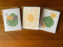 Load image into Gallery viewer, Three stationery cards in distinct linocut designs of green, yellow and purple: a basket made of two leaves, holding three skeins and a pair of knitting needles; a skein of yarn with an unraveling strand prickling with small leaves, or vegetable matter; and a skein with a flower behind it.
