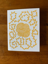 Load image into Gallery viewer, A card with a linocut design depicting a yellow skein of yarn and an unraveling strand prickling with small leaves, or vegetable matter.
