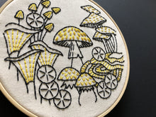 Load image into Gallery viewer, An embroidery hoop holds a finished embroidered piece of mushrooms in black and yellow threads.
