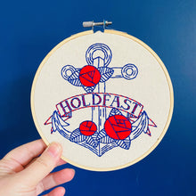 Load image into Gallery viewer, A small round embroidery hoop holds a design in red and blue threads of an anchor decorated with roses and a banner with the words &quot;Hold Fast.&quot;
