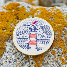 Load image into Gallery viewer, a small circular embroidery in blue and red threads of a round lighthouse and clouds
