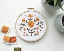 Load image into Gallery viewer, A 5&quot; embroidery hoop holds a stitched design of orange marigolds on green stems.
