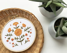 Load image into Gallery viewer, A 5&quot; embroidery hoop holds a stitched design of orange marigolds on green stems.
