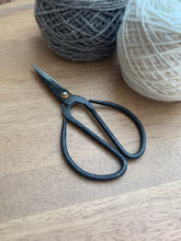Load image into Gallery viewer, A carbon steel 6&quot; bonsai-style scissor next to gray and white skeins of yarn.
