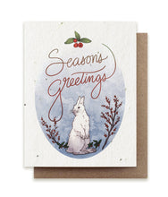 Load image into Gallery viewer, A greeting card made of seed paper shows an illustration of a white snowshoe hare surrounded by holly branches and the words &quot;Season&#39;s Greetings&quot; in cursive over his head.
