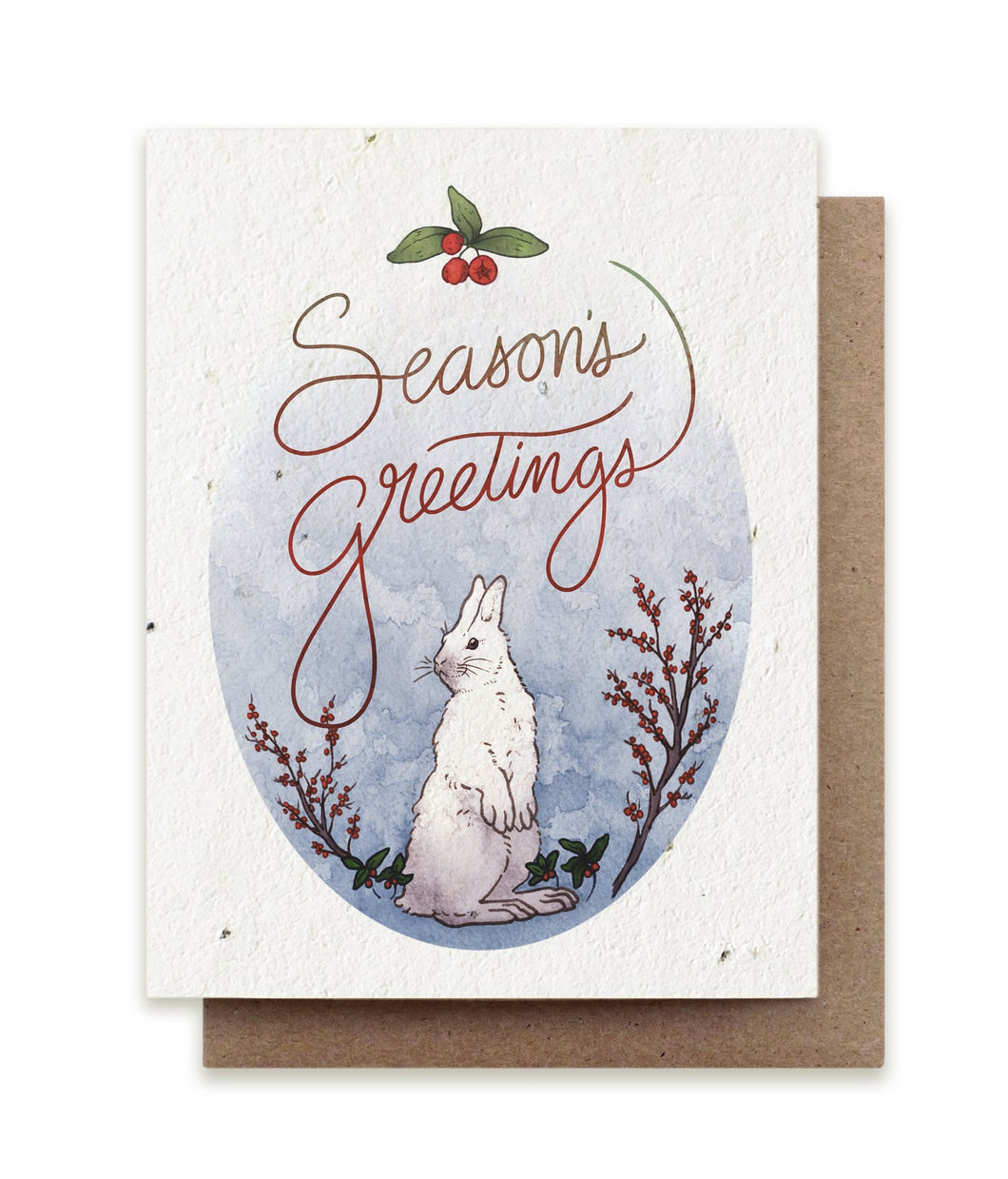 A greeting card made of seed paper shows an illustration of a white snowshoe hare surrounded by holly branches and the words 