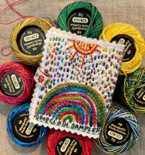 Load image into Gallery viewer, A small needlebook stitched with a strawberry and rainbow design, surrounded by spools of perle cotton thread.
