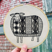 Load image into Gallery viewer, A hand holds a small embroidery hoop with an embroidered picture of a sheep wearing a cable knit sweater, in black embroidery thread.
