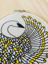 Load image into Gallery viewer, A small round embroidery hoop holds a black and yellow trumpeter swan with a curved wing.
