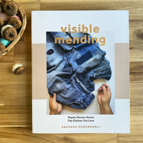 The book Visible Mending sits on a table next to a bowl of wool felted acorns.