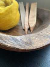 Load image into Gallery viewer, The corner of a carved wood bowl holding several wood tapestry weaving tools and a bump of mustard yellow wool roving.
